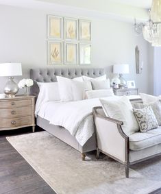 a bed with white linens and pillows in a large room next to a chandelier