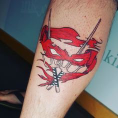 a man's leg with a red and black tattoo design on it, which has two crossed swords in the center