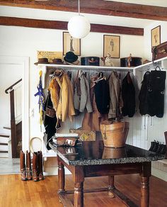 a room filled with lots of coats and shoes on top of a wooden table in front of a white wall