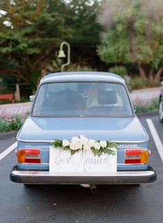 a blue car parked in a parking lot with white flowers on the tailgate and just married sign