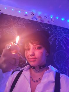 a woman holding a lit candle in her right hand and looking at the camera while wearing suspenders