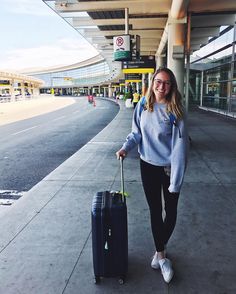 a woman is walking with her luggage at the airport and she is smiling for the camera