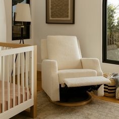 a white rocking chair next to a baby crib in a room with large windows