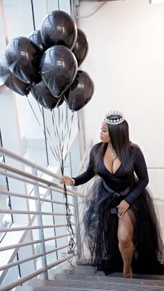 a woman in a black dress is holding some balloons on the stair case while wearing a tiara