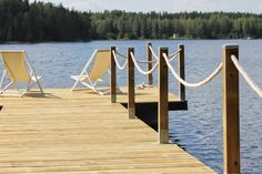 two lawn chairs sitting on a wooden dock next to the water with ropes in front of them