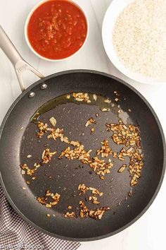 a skillet filled with food next to bowls of rice and tomato sauce on a white table