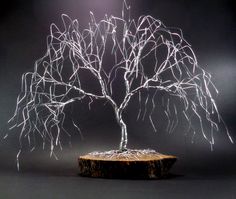 a wire tree sculpture sitting on top of a piece of wood with light coming from behind it