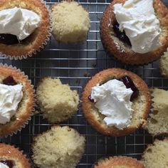 several cupcakes with white frosting and jam on top sitting on a cooling rack