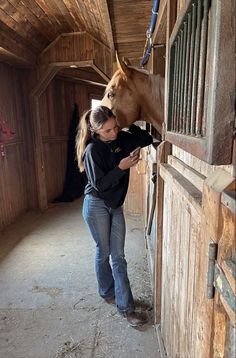 a woman is petting a horse in an enclosed area with wooden walls and beams