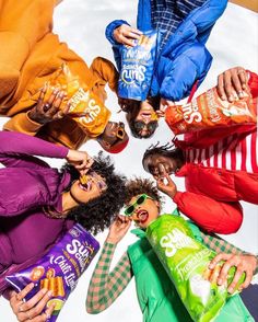 several people standing in a circle holding bags of chips and smiling at the camera with their mouths open