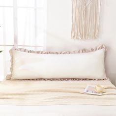 a white bed with a tasseled pillow on it's side and a plant in the corner