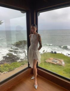 a woman standing in front of a window next to the ocean