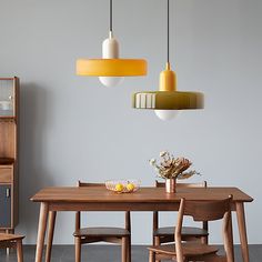 a dining room table and chairs with two pendant lights above it, in front of a gray wall