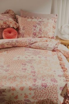 a bed with an orange pillow and pink comforter on it in a white room