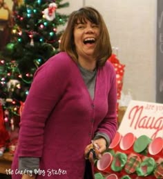 a woman standing in front of a christmas tree holding a pair of scissors and smiling