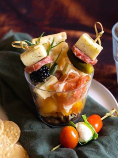 a glass bowl filled with food next to crackers and tomatoes on a tablecloth