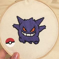 someone is holding up a embroidery project with an image of a pokemon ball on it