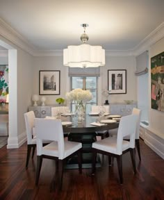 a dinning room table with white chairs and pictures on the wall behind it,