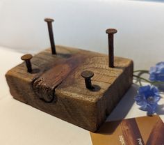 a wooden block with two nails on it next to a credit card holder and flowers