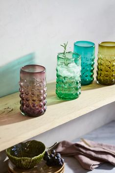 four different colored glass vases sitting on a shelf next to plates and napkins