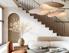 an elegant living room with modern furniture and lighting fixtures on the ceiling, in front of a staircase