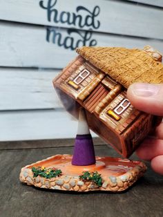 a hand holding a miniature house made out of clay