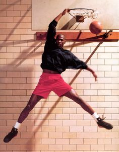 a man in black shirt and red shorts playing with a basketball on a wall mounted hoop