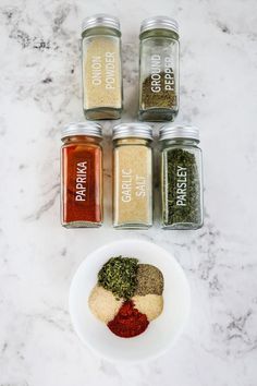 five spices in small glass jars on a marble counter top