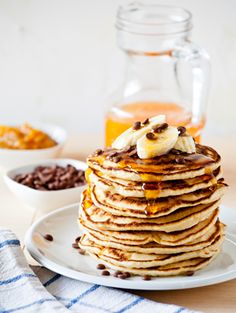 a stack of pancakes sitting on top of a white plate next to a bowl of chocolate chips