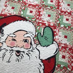 a quilted santa clause holding a green object in his right hand and smiling at the viewer