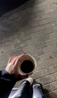 a woman holding a cup of coffee on top of a brick floor next to a sidewalk