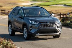 a gray toyota rav driving down a road next to a green golf course in the background