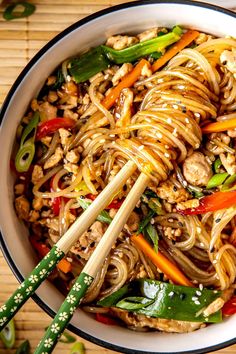 stir fry noodles with chicken and vegetables in a white bowl next to chopsticks