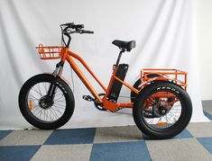 an orange electric bike on display in front of a white wall and blue checkered floor