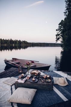 a picnic table with food on it next to a boat in the water at sunset