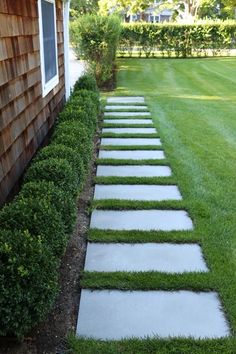 a walkway made out of stepping stones in the grass next to a wooden building with a window