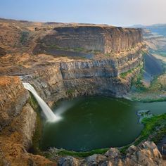 a large waterfall is coming out of the side of a cliff into a body of water