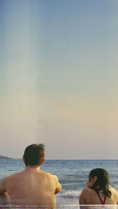 two people sitting on the beach looking out at the ocean