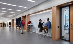 people are sitting at tables in an open office space with glass walls and wooden doors