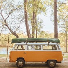 an orange and white van with a surfboard on the roof is parked in front of trees