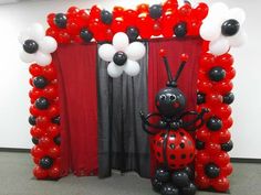 a ladybug balloon arch in front of a red curtain and black and white balloons