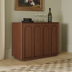 a wooden cabinet with two wine glasses on it and a painting hanging above the door