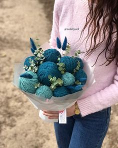 a woman holding a bouquet of blue balls of yarn and greenery in her hands