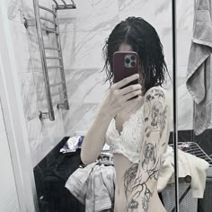 a woman taking a selfie in front of a bathroom mirror with tattoos on her body