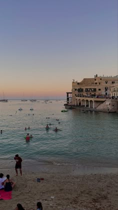 many people are swimming in the water and on the beach at sunset or sunrise time