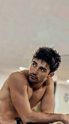 a shirtless man leaning on a table with his hand on his hips and looking at the camera