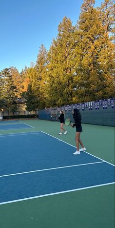 two people playing tennis on a blue court with trees in the backgrouds