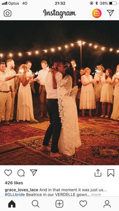 a bride and groom share their first dance as guests look on in the background with string lights