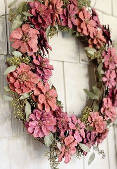 a wreath with pink flowers and greenery hanging on a brick wall in front of a white tiled wall