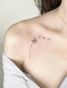 a woman with a small tattoo on her chest and shoulder, holding a dandelion